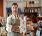 An elderly owner of a home decoration store exudes confidence as he stands in his store with arms crossed and a welcoming smile. His presence reflects the experience and success built over years in the retail industry. Showcases his commitment to quality, sustainable practices, and customer satisfaction.
