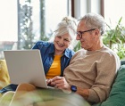 Senior couple using laptop while sitting on sofa in living room at home