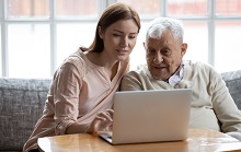 Grown-up daughter and old 80s father choose goods or services via internet or web surfing together at home. Younger generation caring about older relatives teaching using computer useful apps concept